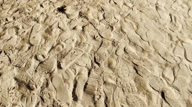Countless shoe prints and tracks cover the soft golden sand from people walking. The messy, layered patterns create a lively, nostalgic feeling of a fun and active day spent by the shore.