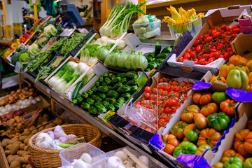 Obraz premium Colorful selection of ripe organic vegetables, including tomatoes, zucchini, and various greens, arranged for sale at an indoor market providing healthy food options