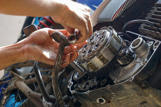 The process of manually repairing or servicing a motorcycle engine by a mechanic. The mechanic's hands are seen removing or installing a cover component near the cylinder block of a two-stroke engine.