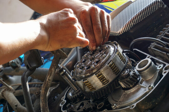 The process of manually repairing or servicing a motorcycle engine by a mechanic. The mechanic's hands are seen removing or installing a cover component near the cylinder block of a two-stroke engine.