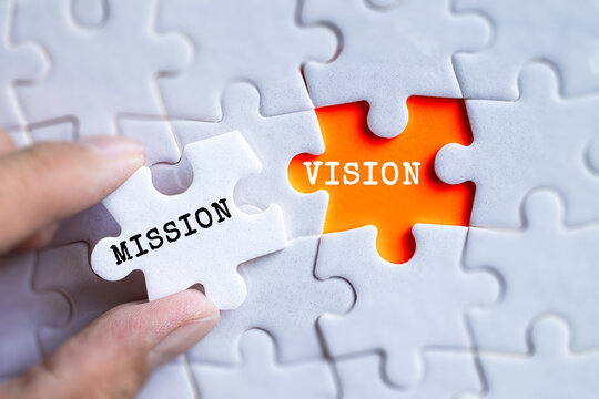 Hand fitting Mission and Vision orange puzzle pieces together on gray jigsaw background, business strategy and corporate planning concept