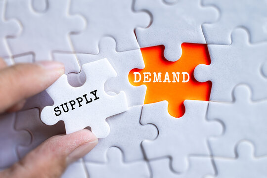 Hand fitting Supply and Demand orange puzzle pieces together on gray jigsaw background, economics and market balance concept