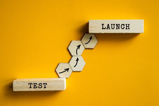 Test and Launch wooden labels with hexagon steps on orange background, software development and product release management concept