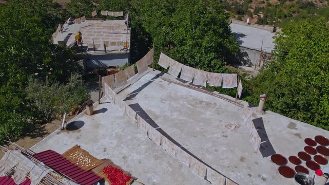 Aerial view of people sun-drying handmade food sheets on a rooftop, showing traditional rural food preparation, summer preservation, community work, and authentic daily life in a warm village setting.