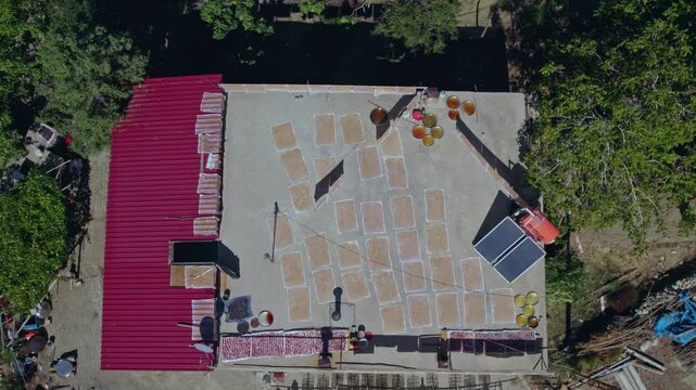 Aerial view of people sun-drying handmade food sheets on a rooftop, showing traditional rural food preparation, summer preservation, community work, and authentic daily life in a warm village setting.