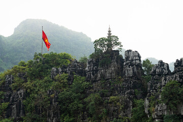 Naklejka premium Vietnamese flag above limestone cliffs in Ninh Binh Vietnam
