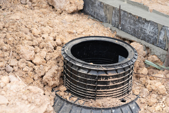 Construction Site Septic Tank: A plastic septic tank lid and base are installed on a construction site, surrounded by loose dirt and a concrete foundation.