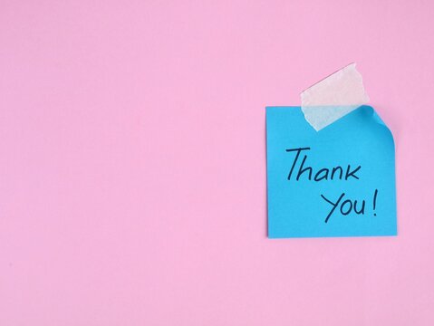 Thank you message handwritten on blue adhesive note taped to pink background. Perfect for concepts of gratitude, appreciation, customer service, and business marketing