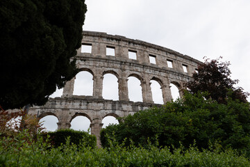 Obraz premium Ancient Roman arena amphitheater in Pula Croatia surrounded by green trees under dramatic cloudy sky view