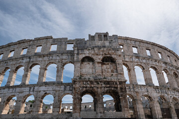 Naklejka premium Front view of ancient Roman amphitheater in Pula Croatia with monumental arches under bright dramatic cloudy sky