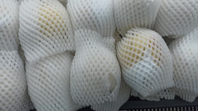 A top-down view of fresh yellow pears neatly wrapped in white protective foam mesh netting on display at a supermarket