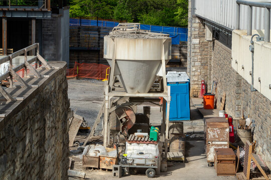 Vibrant outdoor construction site featuring a prominent concrete mixing silo, heavy machinery, and raw building materials under bright sunlight, surrounded by sturdy stone walls and temporary safety