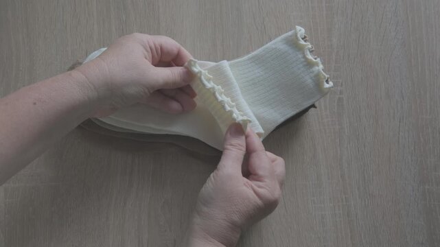 Female hands check cotton socks for quality, meticulous inspection footwear, Elastic bands and fabric texture. Diabetic-friendly apparel. Clothing purchase
