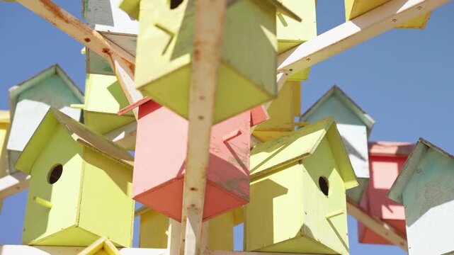 Numerous colorful wooden birdhouses attached to a metal structure, creating a unique art installation against a clear blue sky. A concept of community, housing, and neighborhood diversity