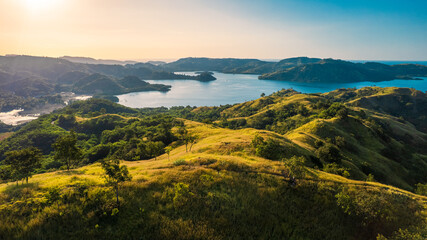 Drone shot of golden savanna hills bordering a quiet tropical bay under a warm sunset sky in Riung 17 Islands National Park.  © Ryan