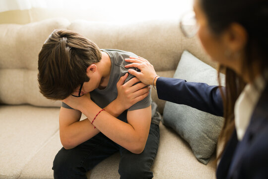 Psychologist comforting sad teenage boy during mental health counseling session, offering support and empathy on sofa