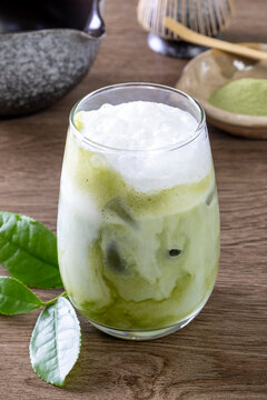 Glass of tasty iced matcha latte, bamboo whisk and powder on grey wooden table, closeup