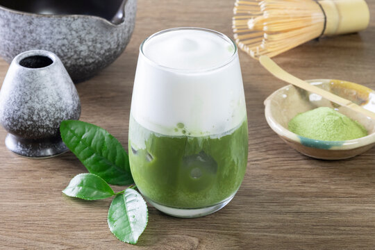 Glass of tasty iced matcha latte, bamboo whisk and powder on grey wooden table, closeup