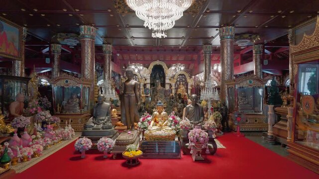 Numerous Buddha images in the hall, flower arrangements, and statues of monks at Wat Pa Daraphirom, Chiang Mai.