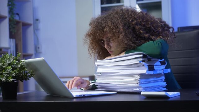 Overworked woman asleep on stack of paperwork at desk while using laptop in office at night, blue light, stress and burnout concept.