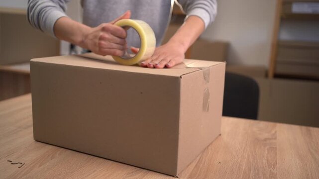 female hands sealing cardboard box with adhesive packaging tape.