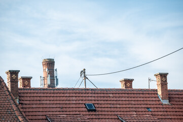 Naklejka premium Ziegeldach mit mehreren eckigen Kaminen aus rotem Backstein und Dachständer für Stromleitung vor blauem Himmel in Nürtingen-Neckarhausen mit Schleierwolken.