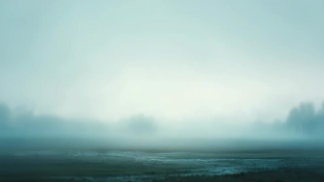 Misty landscape at dawn with soft blue tones and blurred silhouettes of distant trees. Tranquil morning fog creates a dreamy, ethereal atmosphere across the open field