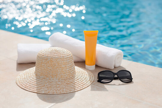 Summer vacation essentials with straw hat, sunglasses, towels and sunscreen by swimming pool