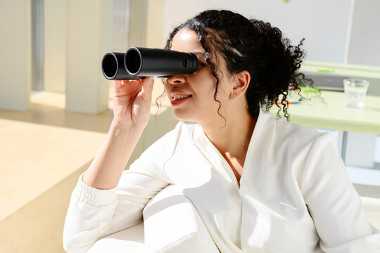 Professional looking through binocular in bright sunny office