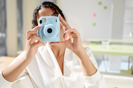 Photographer holding light blue instant camera in bright office