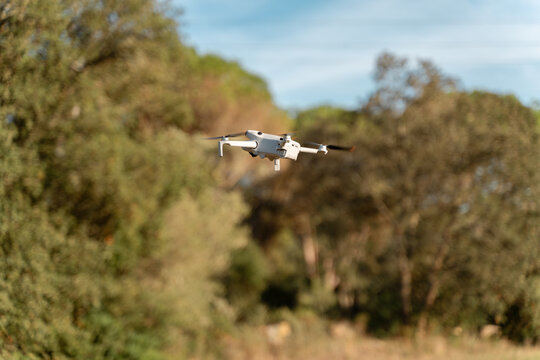 White drone flying in the air against blurred green nature background