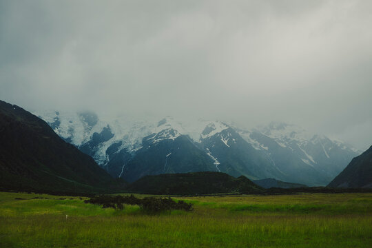 Moody snow capped mountain over green meadow in New Zealand