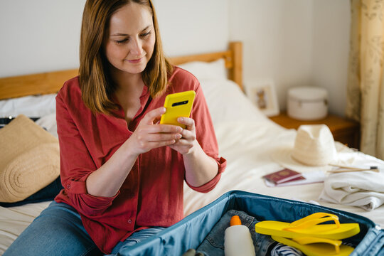 Tourist packing suitcase for summer vacation and using smartphone