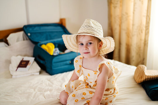 Little girl sitting on bed with suitcase preparing for summer vacation