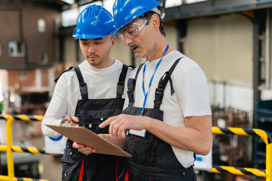 Factory worker discussing plan on clipboard with supervisor
