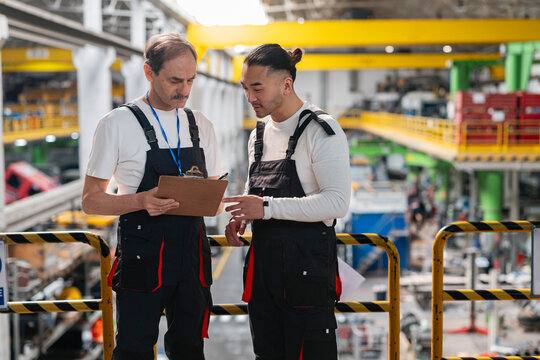 Factory personnel discuss production plan on clipboard indoors