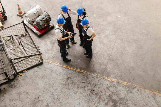Mechanics discussing project over tablet on warehouse floor