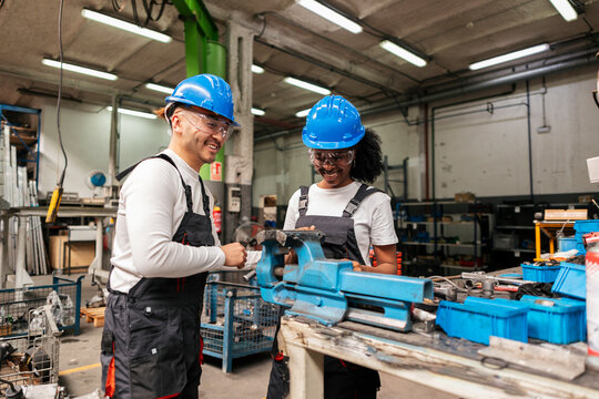 Mechanics wearing helmets talk at indoor factory workbench