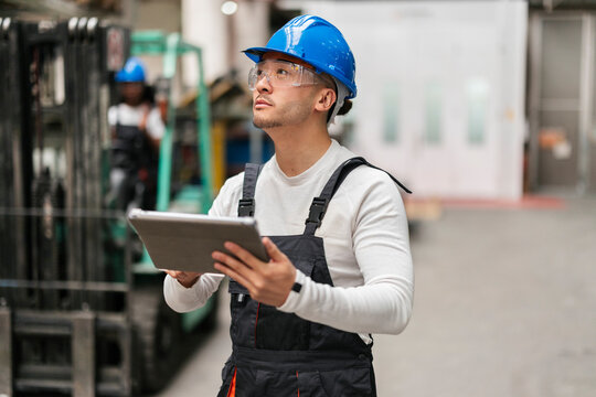 Factory inspector in hard hat holding a digital tablet indoors