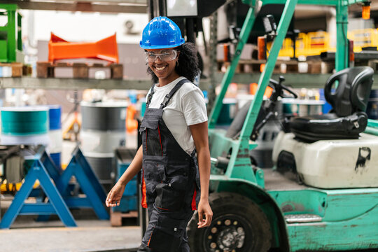 Smiling worker in safety helmet walking through industrial warehouse