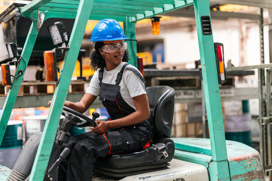 Worker driving a forklift backwards in an industrial warehouse