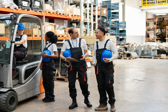 Warehouse team discussing operation by forklift indoors