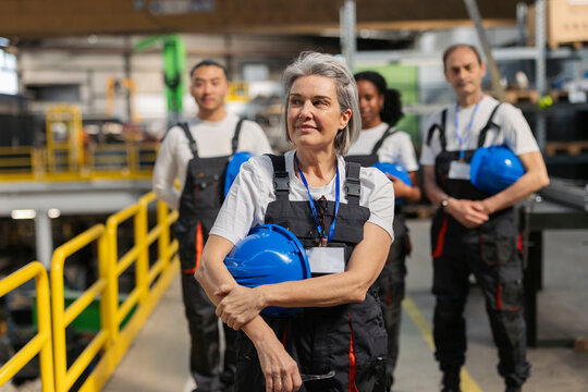 Smiling factory leader holding blue helmet standing indoors