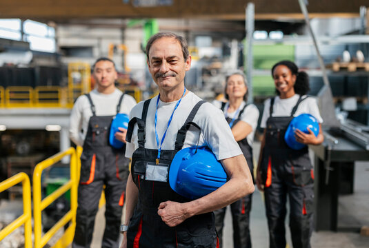 Smiling industrial worker holding hard hat with team in factory