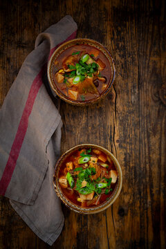 Two bowls of spicy kimchi soup with tofu on a rustic wooden table