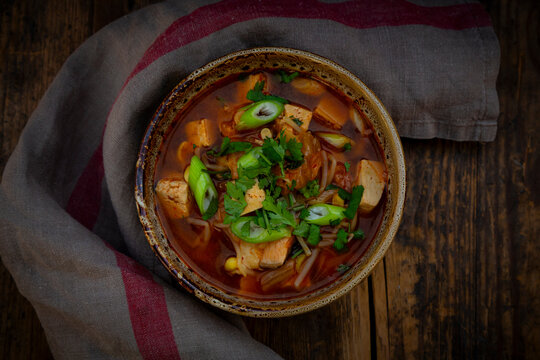 Spicy Korean kimchi soup with tofu and cilantro on a wooden table