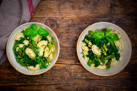 Green spring minestrone with asparagus and pasta on a wooden table