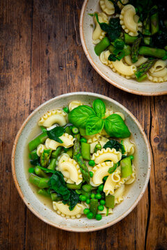 Green spring minestrone soup with pasta on dark wood