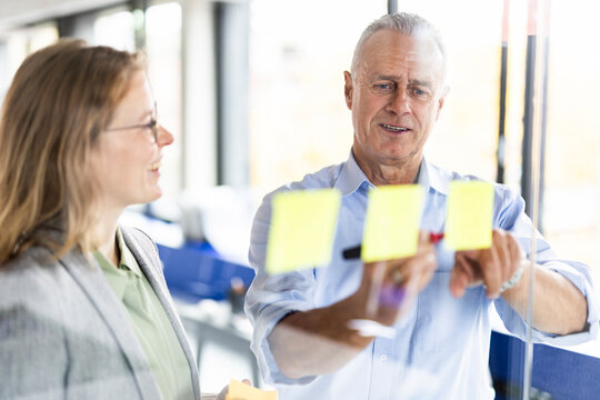 Senior businessman writing on adhesive note at glass wall in office