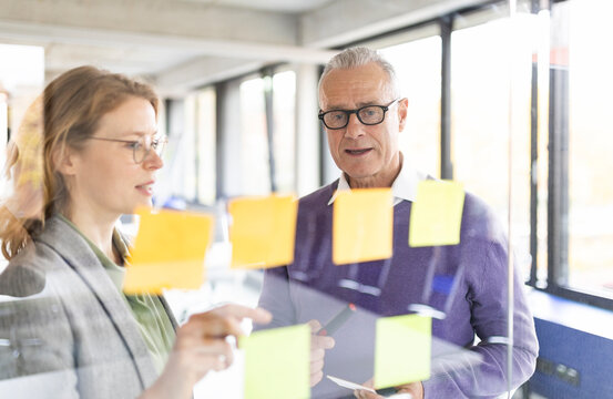 Businessman wearing eyeglasses discussing ideas with coworker near glass wall
